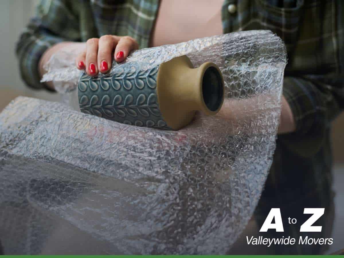 Person wrapping a ceramic vase in bubble wrap, showing the use of protective packing materials during a move