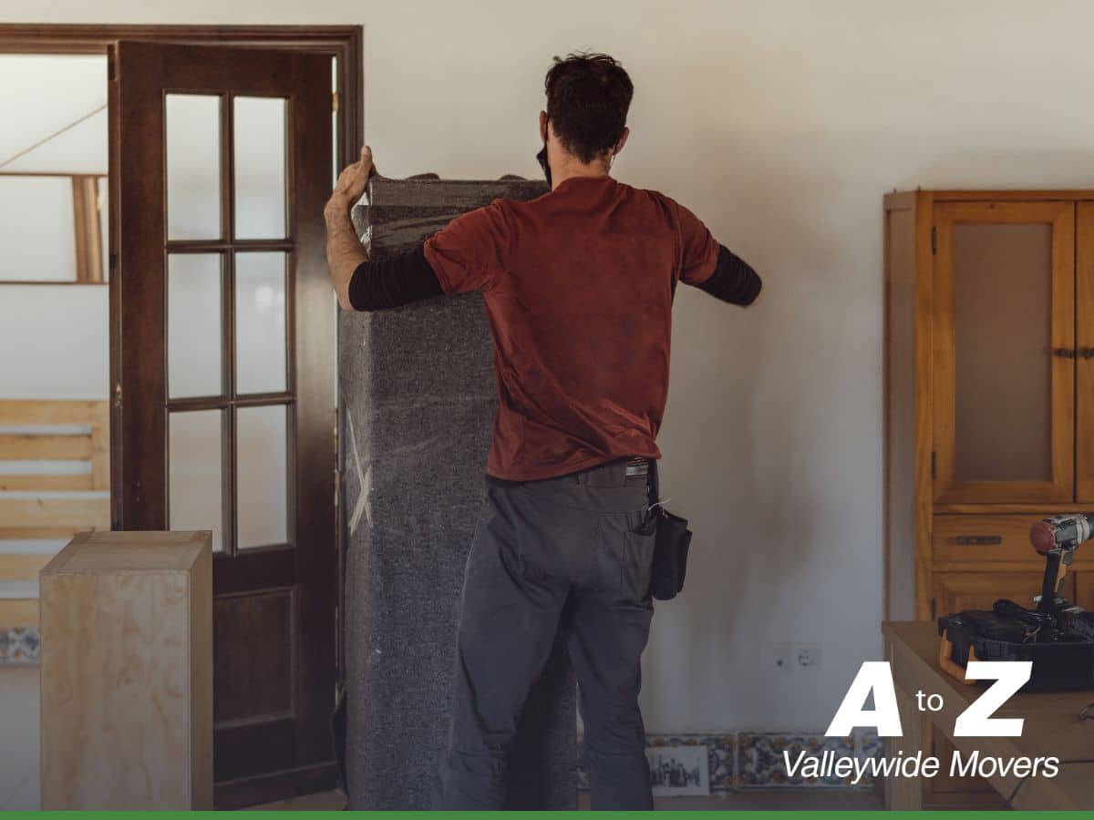 A professional mover from A to Z Valleywide Movers carrying wood furniture wrapped in protective blankets.