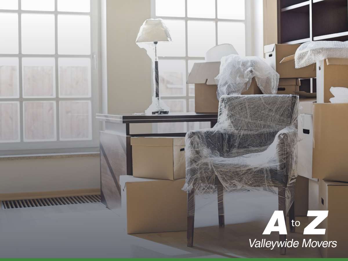 A room during moving process with furniture and boxes wrapped for protection, featuring the text 'A to Z Valleywide Movers' highlighting Packing & Unpacking Services.