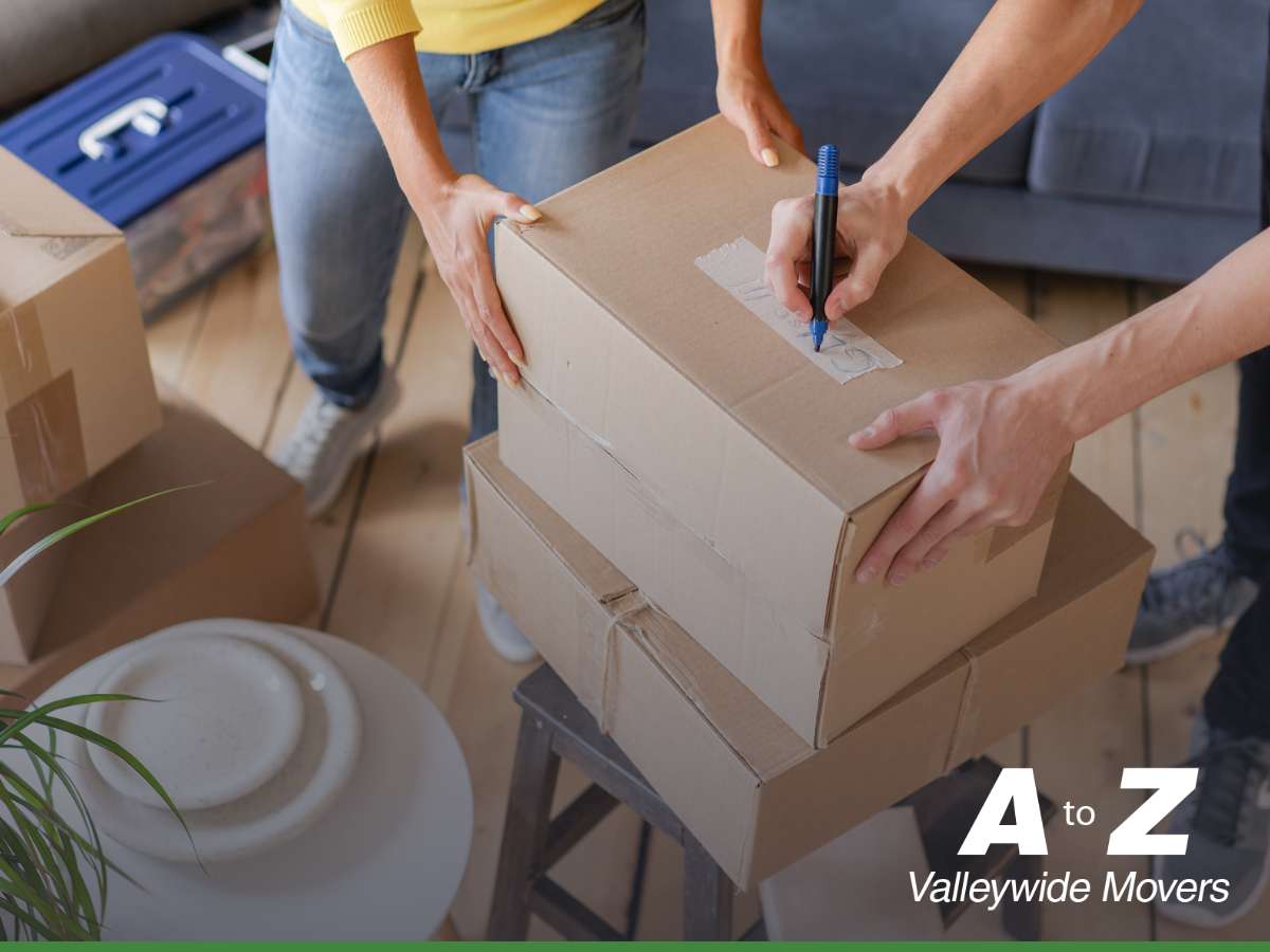 A couple organizing and labeling boxes to efficiently prepare their home before the movers arrive, with the A to Z Valleywide Movers logo displayed